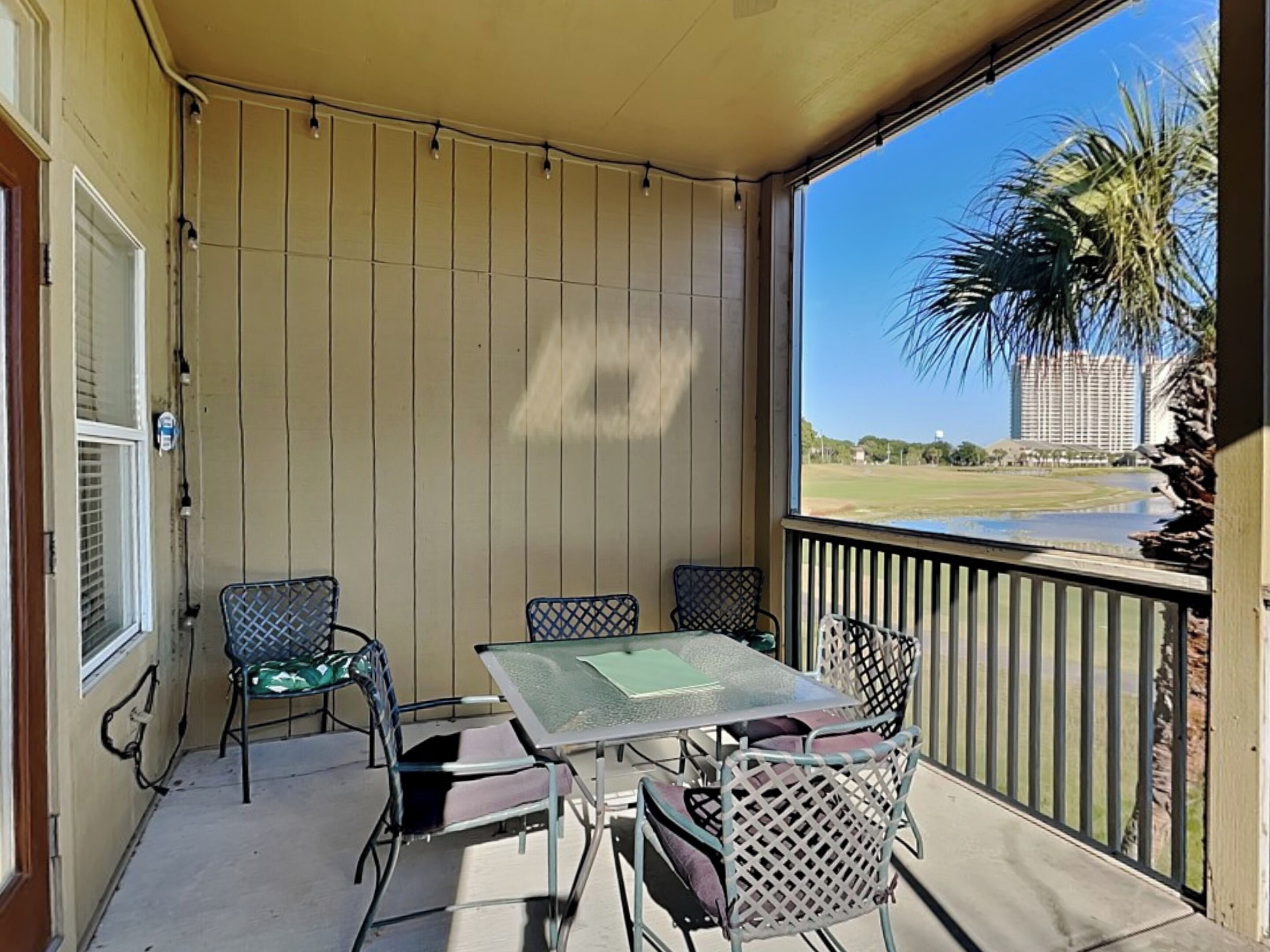 A covered outdoor area with a table and chairs, a view of a palm tree and a building in the background.