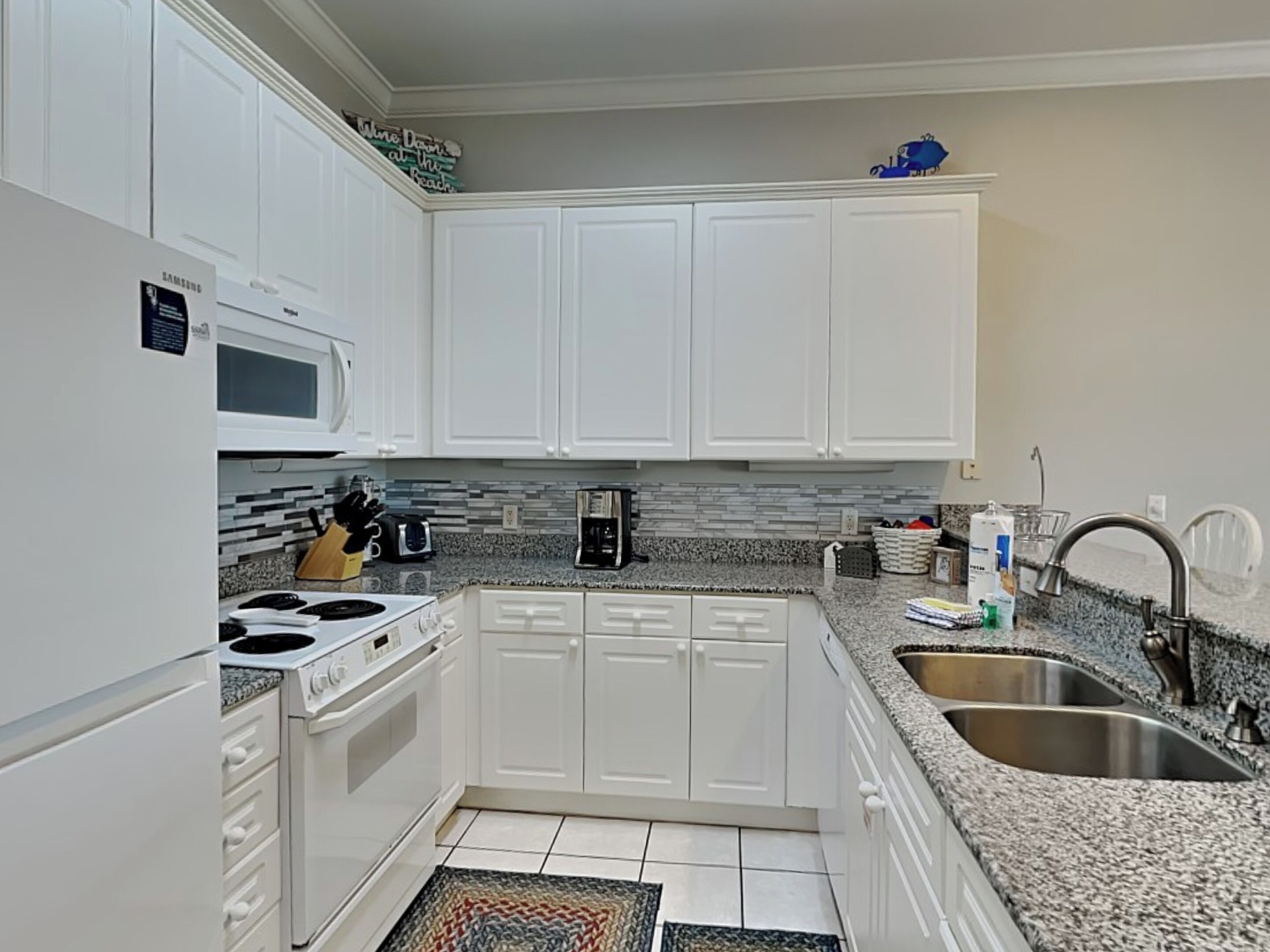 A modern kitchen with white cabinets, a built-in microwave, a stove, a coffee maker, and a sink.