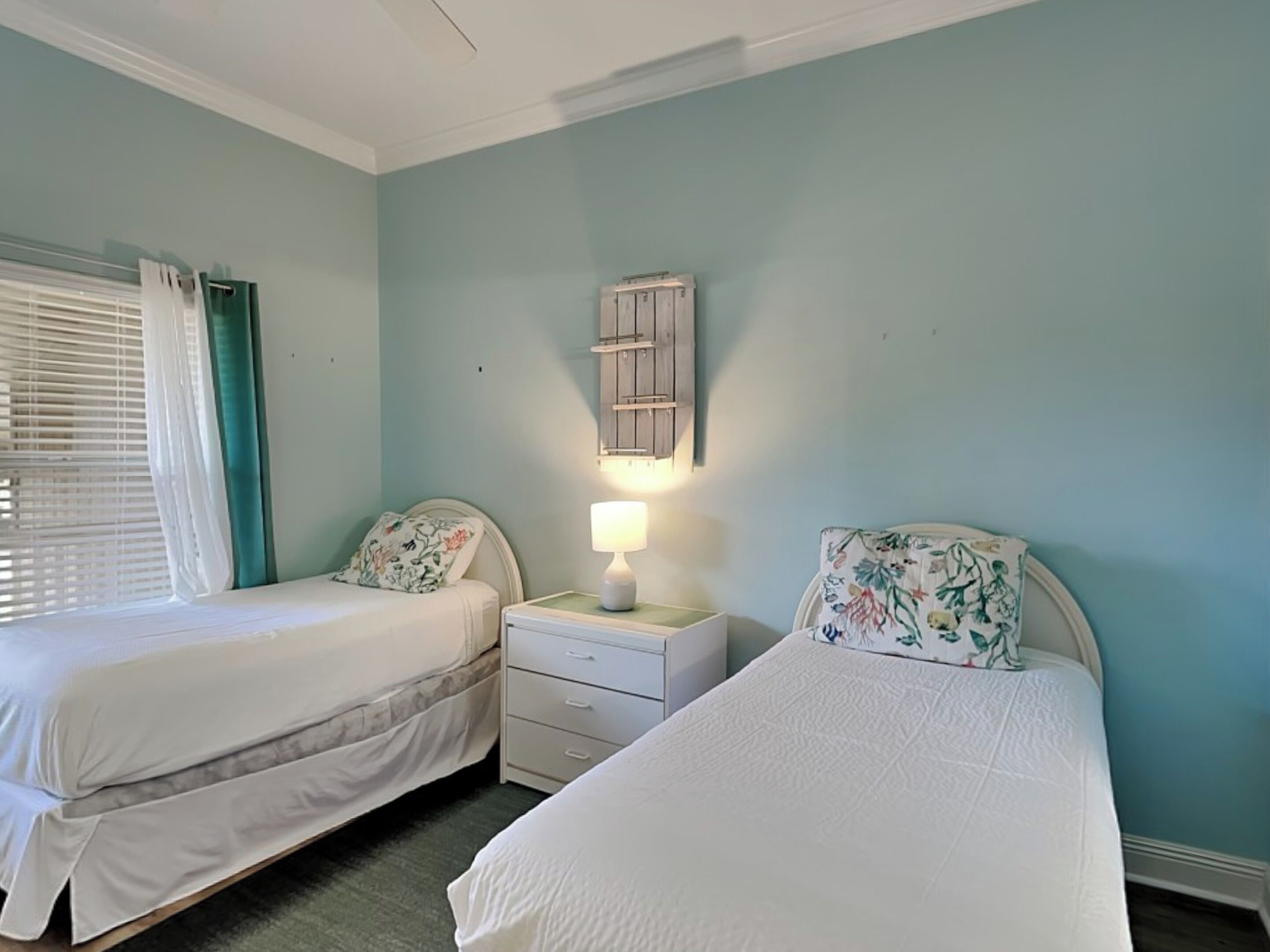 A bedroom with two beds, a nightstand with a lamp, and a window with curtains.