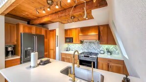 A modern kitchen with wooden cabinets, a stainless steel refrigerator, a gas stove, and a white countertop. - Spacious Mid Century 3 bed 3 bath with Hot Tub! (Breckenridge)