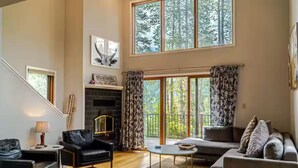 A spacious living room with a fireplace, a sofa, a chair, and a large window offering a view of trees. - Spacious Mid Century 3 bed 3 bath with Hot Tub! (Breckenridge)
