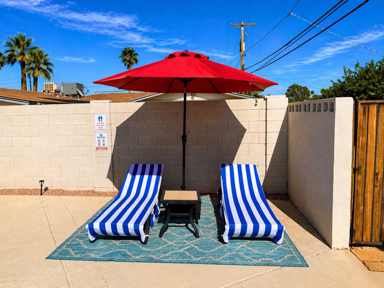 Een terras met twee gestreepte loungestoelen, een rode parasol en een kleine tafel.