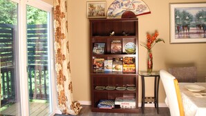 A dining area with a table set for two, a bookshelf with cookbooks, and a view through a glass door. - Bright 3-bedroom house with full kitchen, fenced yard and sports court (Mountlake Terrace)