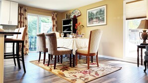 A dining area with a table set for four, chairs, a bookshelf, and a window with curtains. - Bright 3-bedroom house with full kitchen, fenced yard and sports court (Mountlake Terrace)
