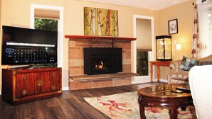 A living room with a fireplace, a television, and a ceiling fan. - Bright 3-bedroom house with full kitchen, fenced yard and sports court (Mountlake Terrace)