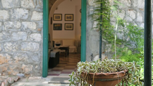 A stone building with a green archway leading to a room with a checkered floor and framed pictures on the wall. - Villa Ariadne - Sea View Sanctuary (Idra)