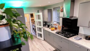 A modern kitchen with grey cabinets, a black stove, and a window with blinds. - Beautiful Wythenshawe Home Near Airport With Garden & Parking Sleeps 5 (Manchester)