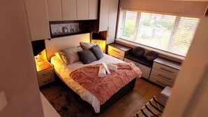 A bedroom with a bed, bedside tables, a window with blinds, and built-in storage cabinets. - Beautiful Wythenshawe Home Near Airport With Garden & Parking Sleeps 5 (Manchester)