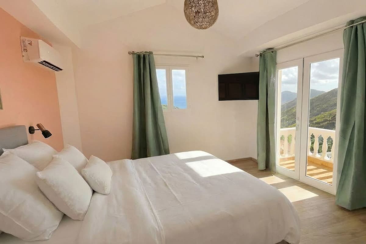 Een slaapkamer met een bed, een aan de muur bevestigde televisie en een balkon met gordijnen.
