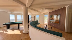 A spacious living area with a pool table, a curved green sofa, and a large window offering a view of the outdoors. - The Pearl of Paradise (Marigot)
