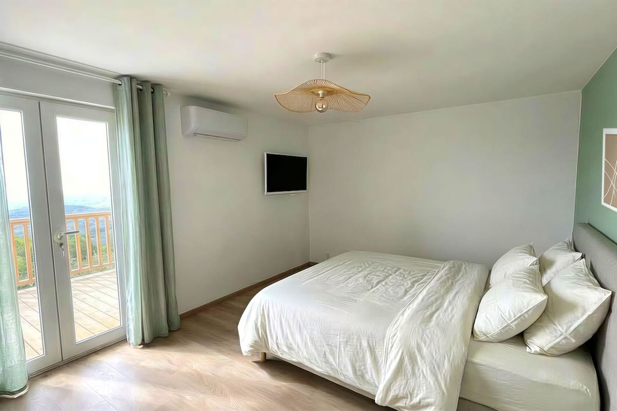 Een slaapkamer met een bed, een plafondventilator, een televisie en een balkon met gordijnen.