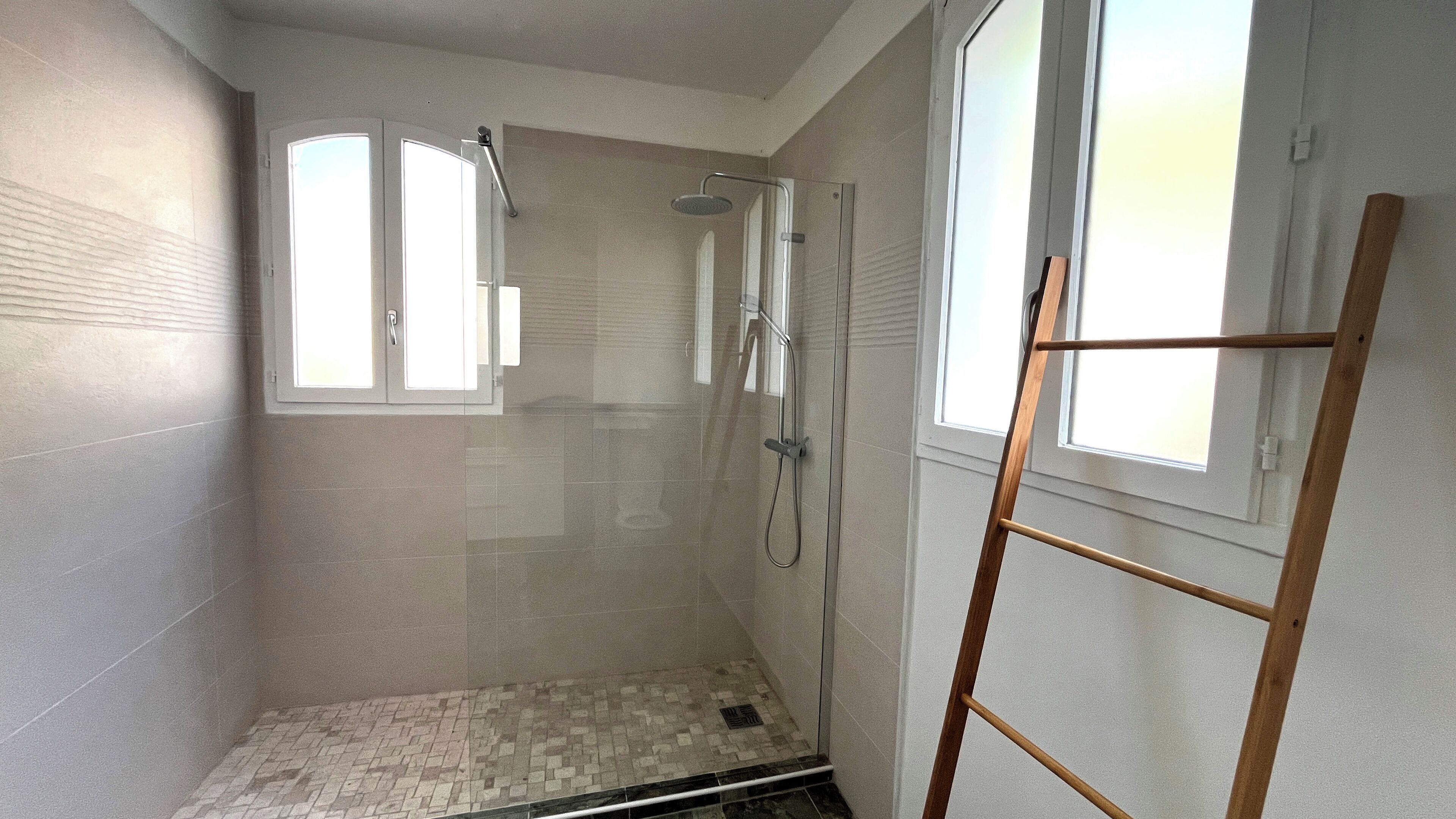 Baño con puerta de vidrio, escalera de madera y ventana.