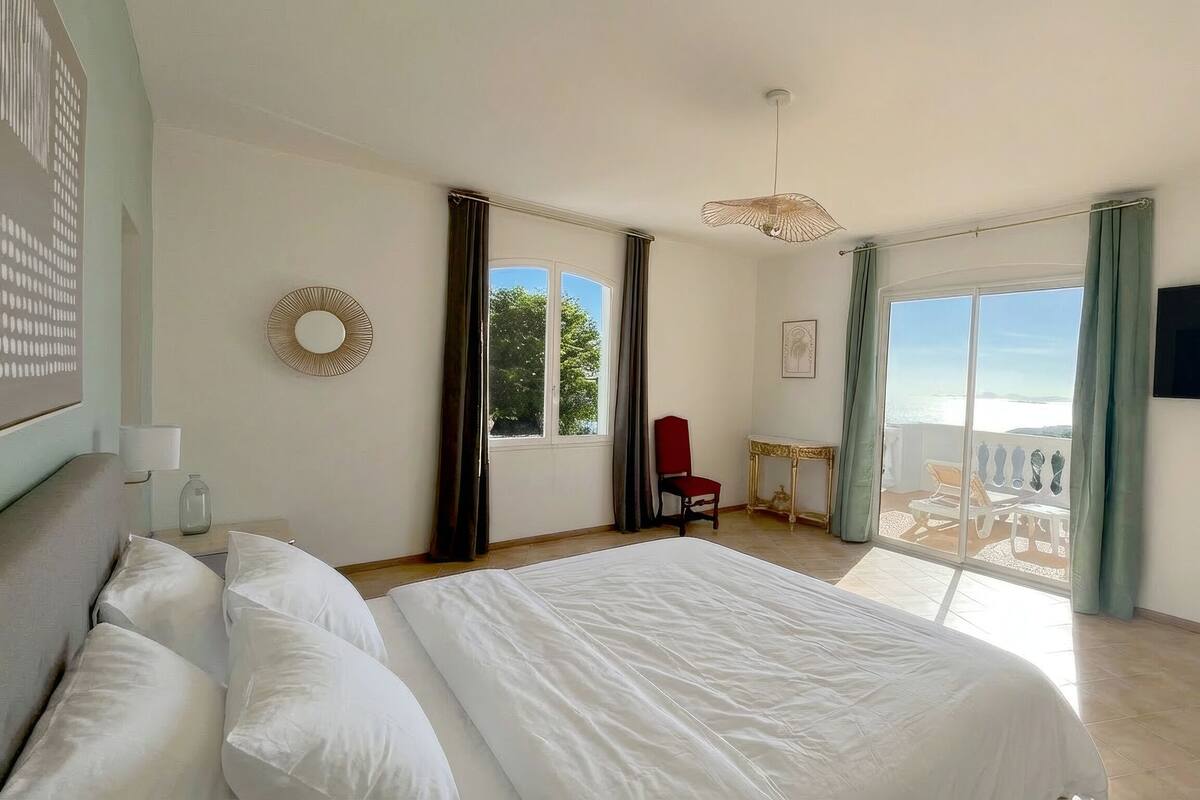 Hotelkamer met een groot bed, een rode stoel, een kleine tafel, een televisie en een balkon met uitzicht op zee.