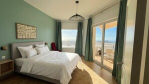 A bedroom with a large bed, a view of the city, and a balcony with a chair. - The Pearl of Paradise (Marigot)