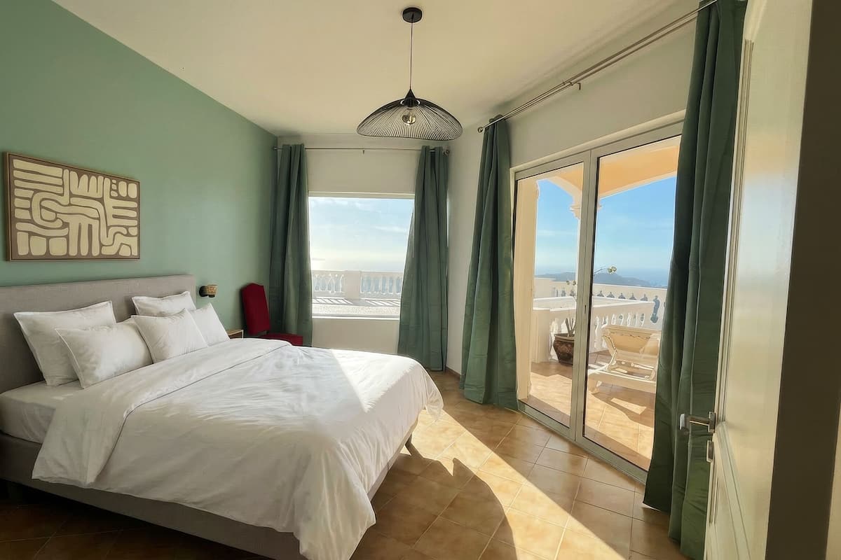 Een slaapkamer met een groot bed, stadszicht en een balkon met een stoel.