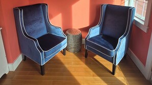 Ein Zimmer mit zwei blauen Sesseln, Holzboden, roter Wand und einem gerahmten Bild.