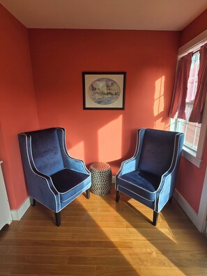 Ein Zimmer mit zwei blauen Sesseln, Holzboden, roter Wand und einem gerahmten Bild.