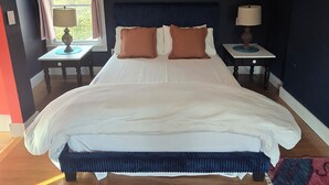 Ein Schlafzimmer mit einem großen Bett, zwei Nachttischen, einem Fenster mit Vorhängen und einem Beistelltischchen mit Lampe.