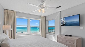 A bedroom with a large bed, a ceiling fan, a TV, and a view of the ocean. - Emerald Dunes 204*Pool*HotTub*Remodeled*Beach Gear (Destin)