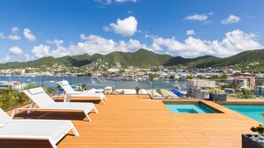 Um deck de madeira com cadeiras de descanso com vista para uma marina e uma cidade.