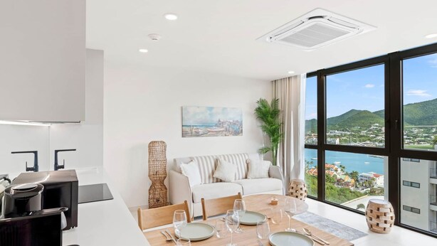 Uma sala de estar moderna com área de jantar, uma janela grande com vista para a paisagem costeira e uma cozinha com cafeteira.