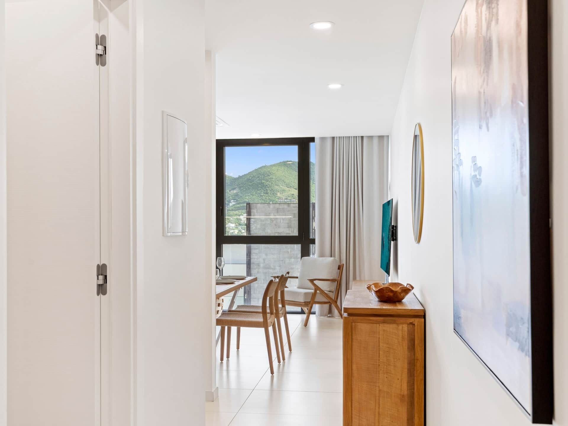 A modern hotel room with a dining area, a large window with a view, and a wooden sideboard.