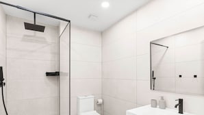 Ein modernes Badezimmer mit einer Duschkabine, einer Toilette und einem Waschtisch mit Spiegel.
