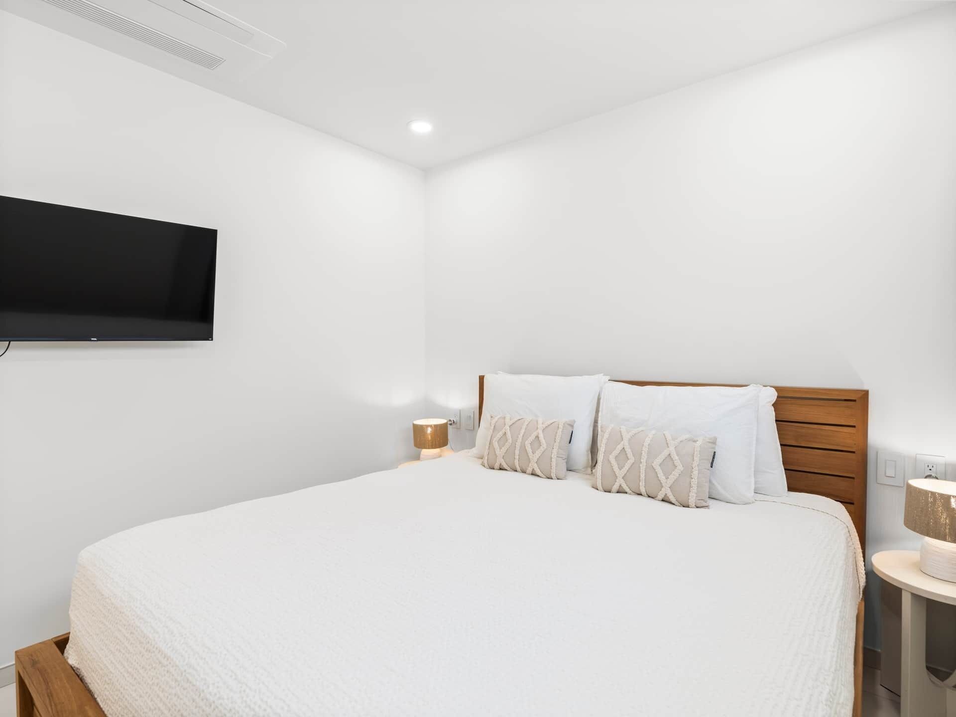 Une chambre à coucher avec un lit, un téléviseur fixé au mur et des tables de chevet.