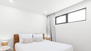 Ein modernes Schlafzimmer mit einem hölzernen Bettgestell, weißer Bettwäsche und einem Nachttisch mit Lampe.