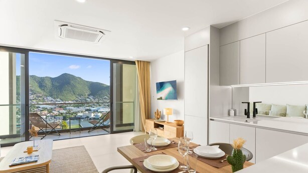 A modern kitchen with a dining area, large windows with a city and mountain view, and a flat-screen TV on the wall. - D432 Very beautiful apartment with a balcony (Cole Bay)