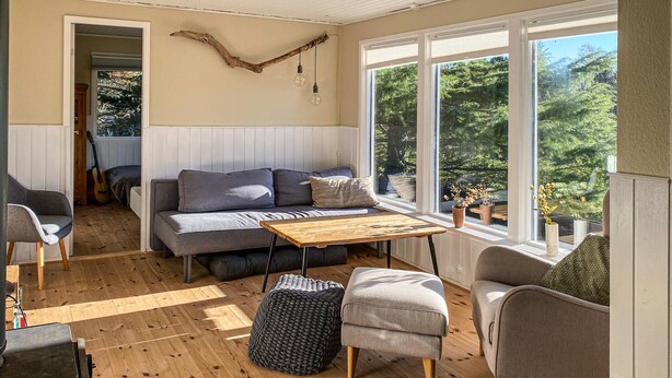 Een gezellige woonkamer met een bank, een houten salontafel en uitzicht op het groen door grote ramen.