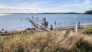 Een steiger die zich uitstrekt over een rustig meer, waar mensen wandelen en zwemmen.