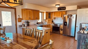 A kitchen with wooden cabinets, a stainless steel refrigerator, and a dining area with a wooden table and chairs. - Peaceful Rustic Mountain Getaway-Aspen Peaks Retreat (Hartsel)