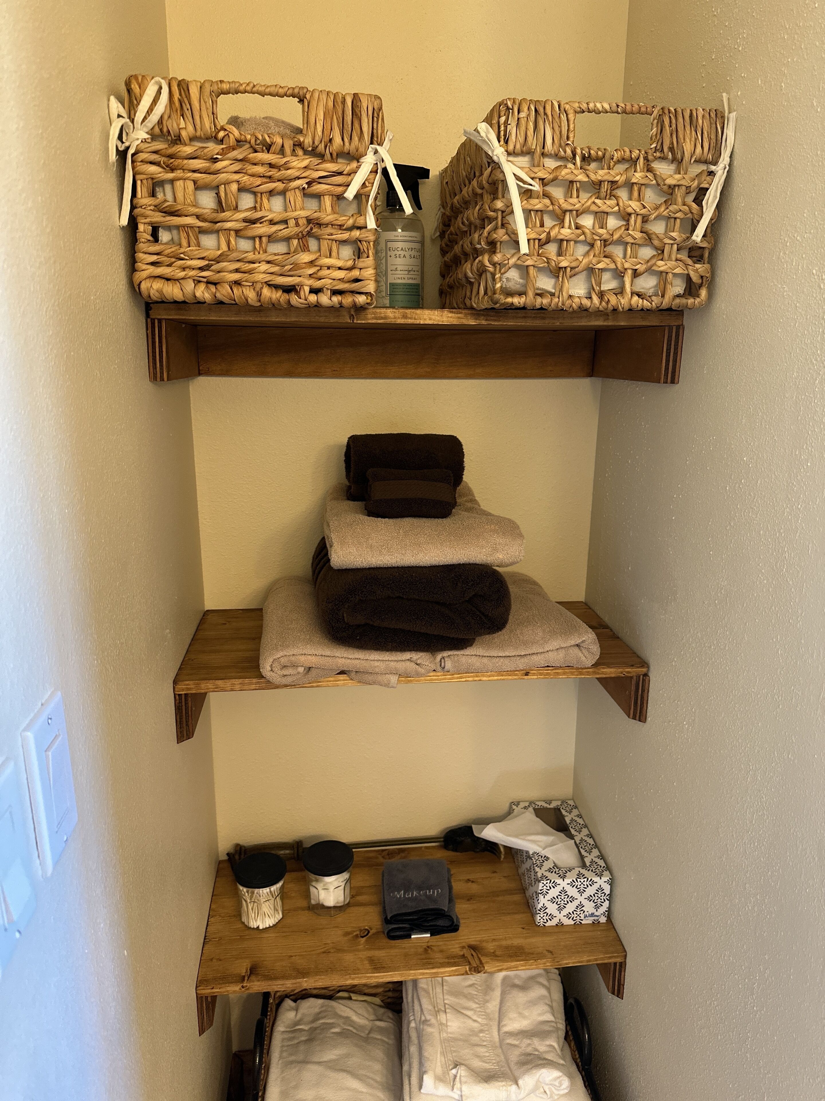 A bathroom with wooden shelves holding towels, a bottle of eucalyptus sea salt, and toiletries.