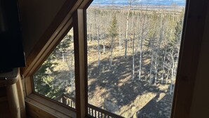 A room with a large window offering a view of a forested landscape. - Peaceful Rustic Mountain Getaway-Aspen Peaks Retreat (Hartsel)