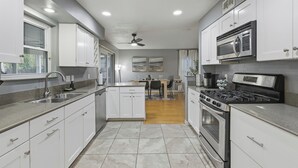 A modern kitchen with white cabinets, stainless steel appliances, and a dining area in the background. - Cozy 5BD/fun house (Austin)