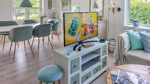 Ein modernes Wohnzimmer mit Fernseher, Essbereich und Blick auf Grünflächen.
