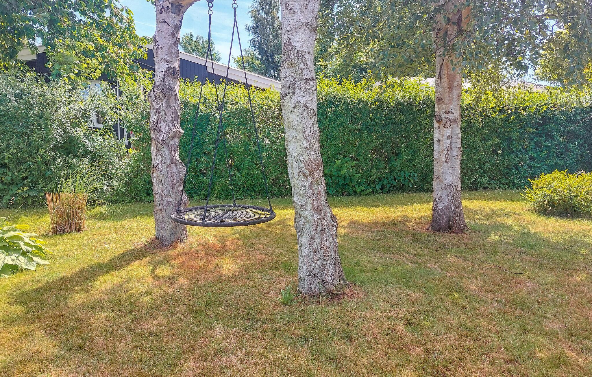 A garden with a swing set, trees, and a hedge.