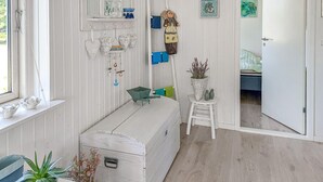 Ein Zimmer mit einer weißen Kommode, einem kleinen weißen Hocker, einem Fenster mit Ausblick und einer Tür zu einem anderen Raum.