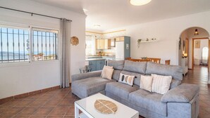 Een woonkamer met een grijze bank, een bijzettafeltje en uitzicht op de keuken en het balkon.