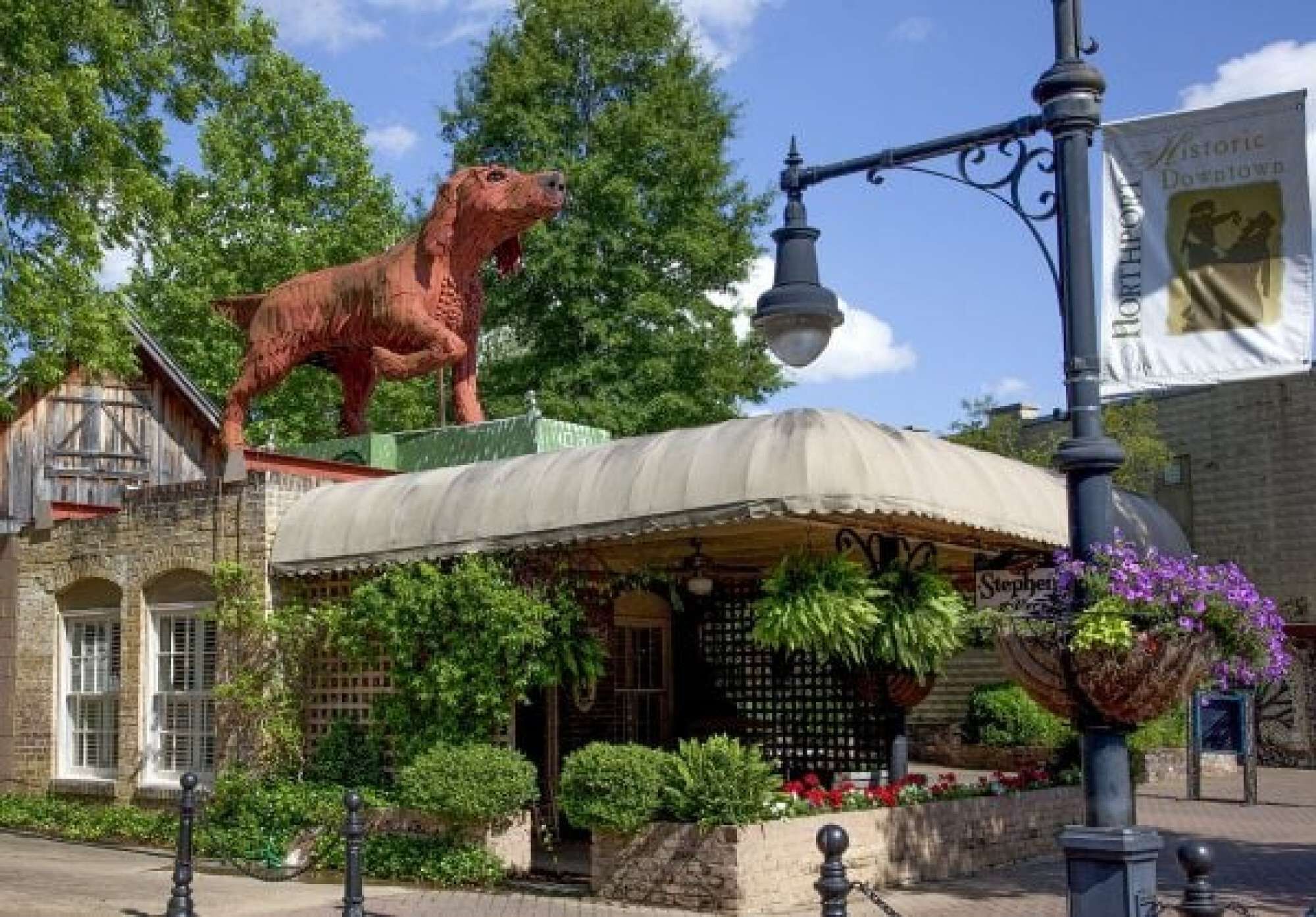 A historic downtown building with a red horse statue, a covered outdoor seating area, and a street lamp.