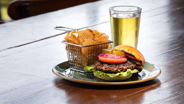 A plate with a burger, fries, and a glass of beer on a wooden table. - Near The University of Alabama + Restaurant & Bar (Tuscaloosa)