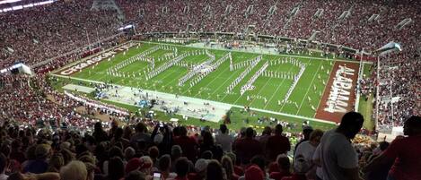 A stadium filled with spectators, featuring a football field with marching band formations.