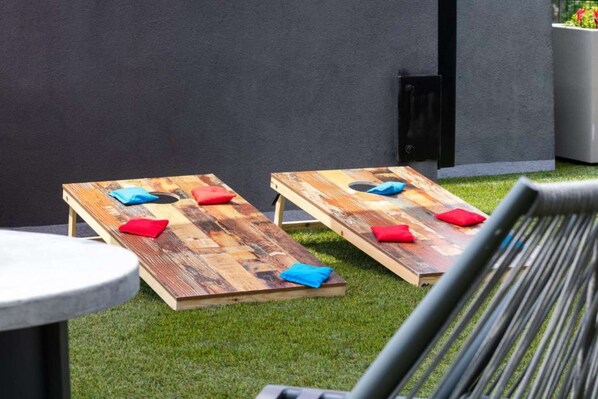 Deux chaises longues en bois avec des coussins, placées sur une pelouse, un mur moderne et un gril en métal au premier plan.