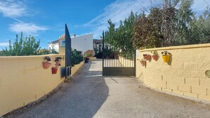 Un chemin mène à une entrée fermée par un portail, et des plantes en pot sont disposées le long des murs.