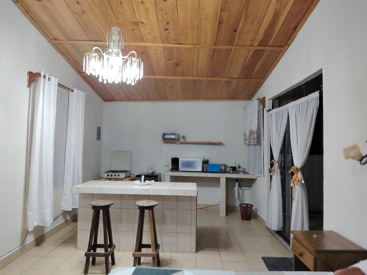 A kitchen with a wooden ceiling, white tiles, a central island with stools, a microwave, and a gas stove.
