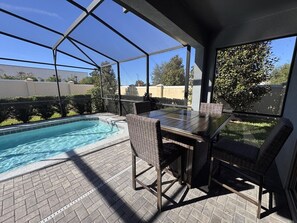 Een overdekt terras met een zwembad, tuinmeubilair en uitzicht op de omgeving.