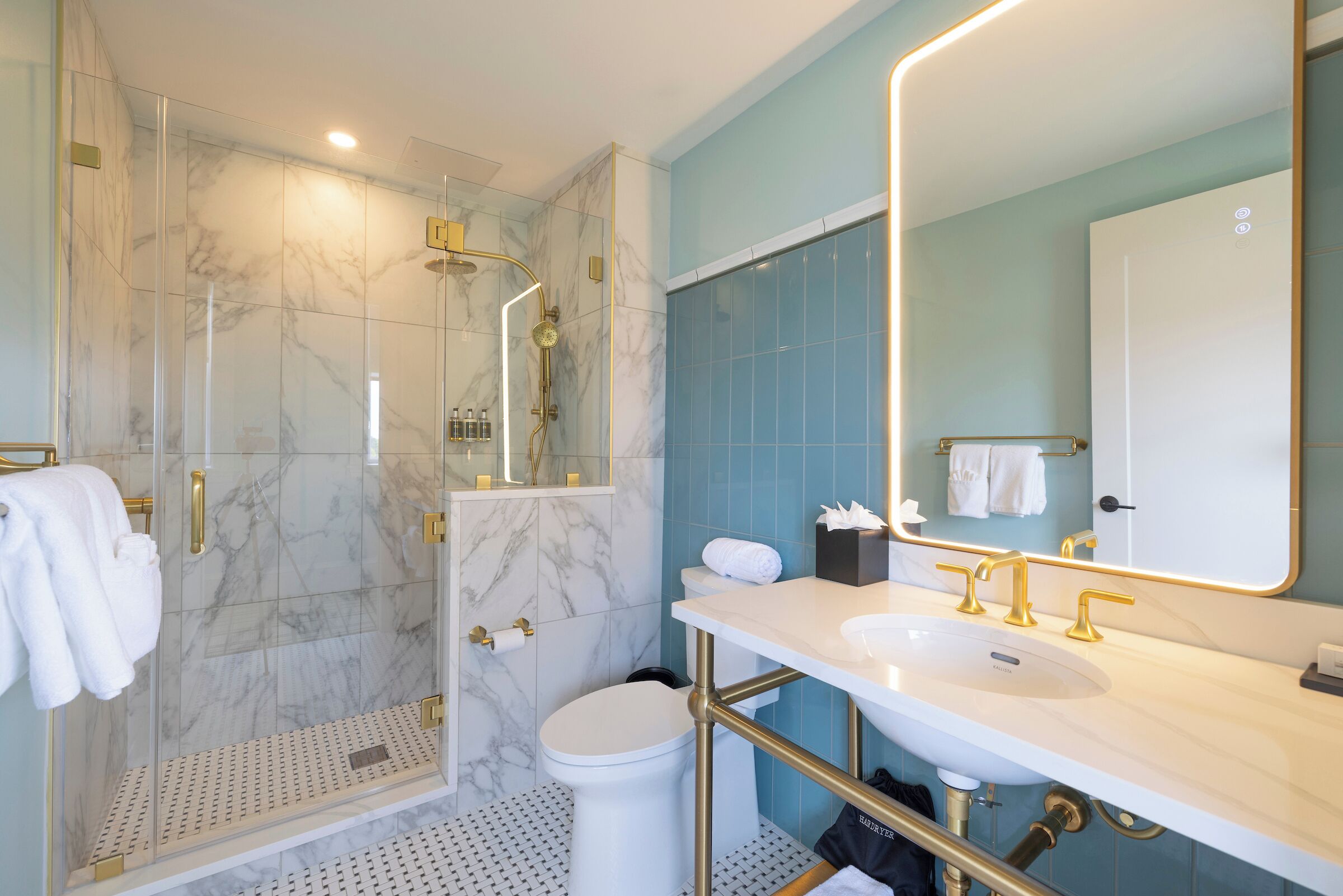 Une salle de bain moderne avec une douche à parois de verre, des toilettes blanches et un lavabo doté de robinetterie dorée.