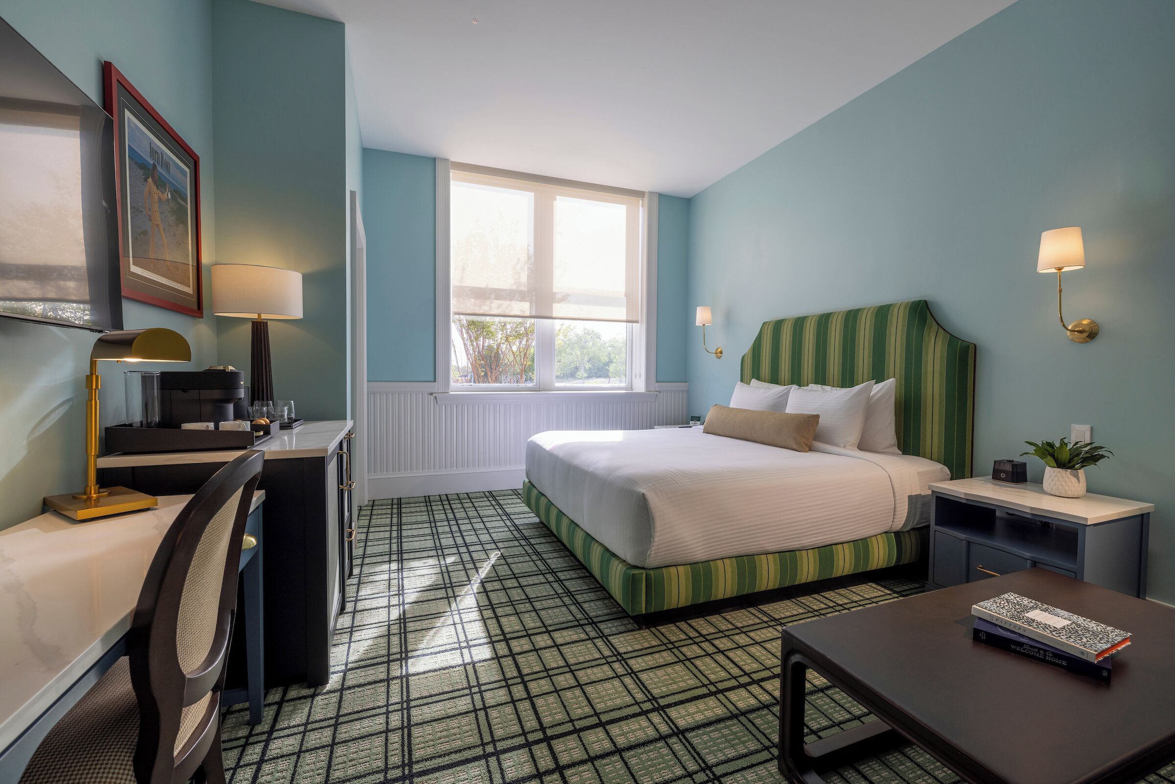 Une chambre d’hôtel comprenant un lit, un bureau, une chaise, une lampe, une table de chevet et une fenêtre.
