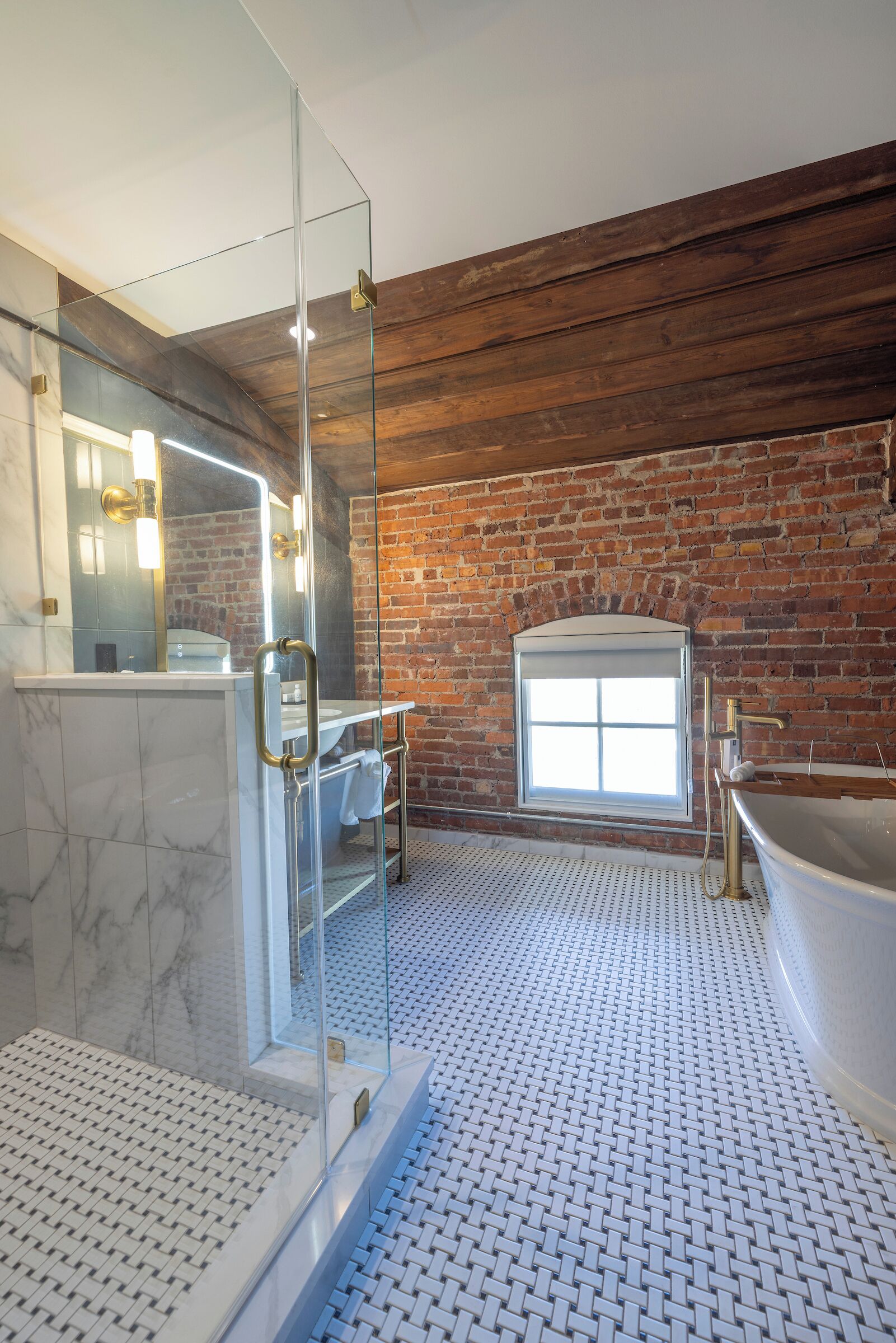 Une salle de bain moderne avec une douche à parois de verre, un grand miroir, une baignoire et un mur en briques.